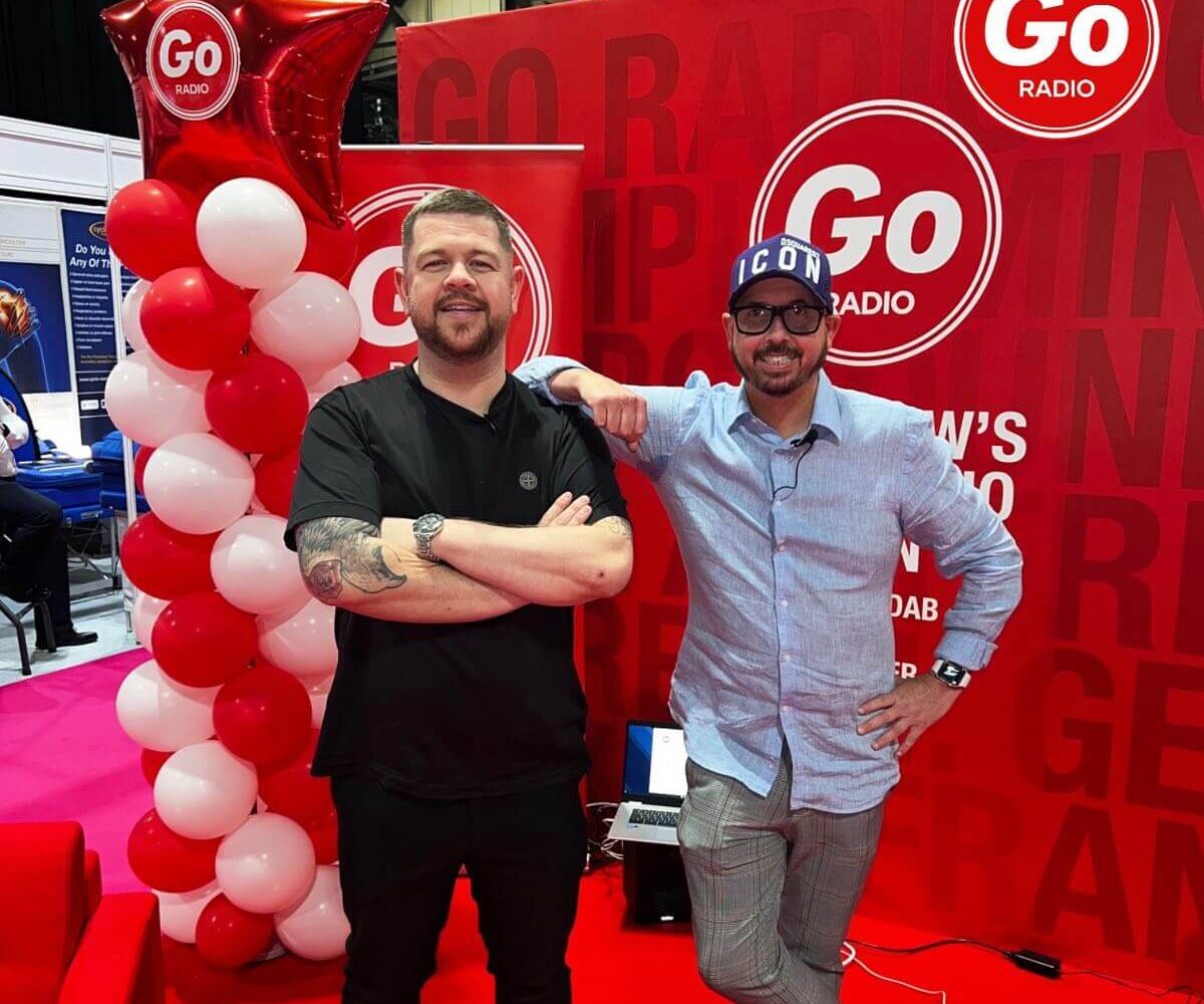Crofty and Grado standing in front of the Go Radio sign